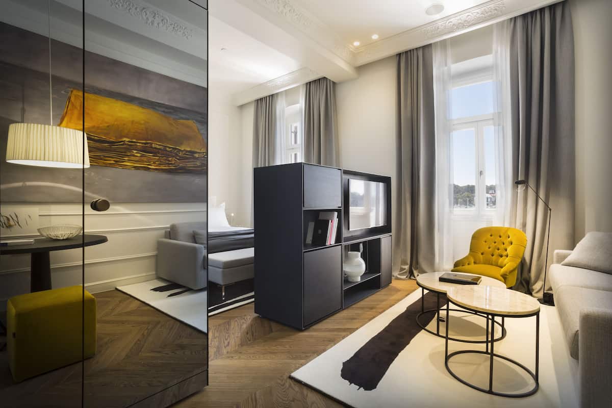 A modern living room with a sofa, a yellow armchair, a coffee table, a TV stand, and a painting on the wall.