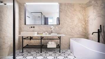 A modern bathroom with a marble wall, a freestanding bathtub, a vanity with a mirror, and a patterned floor.