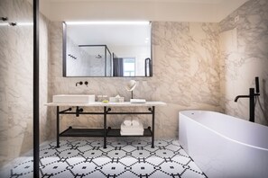A modern bathroom with a marble wall, a freestanding bathtub, a vanity with a mirror, and a patterned floor.