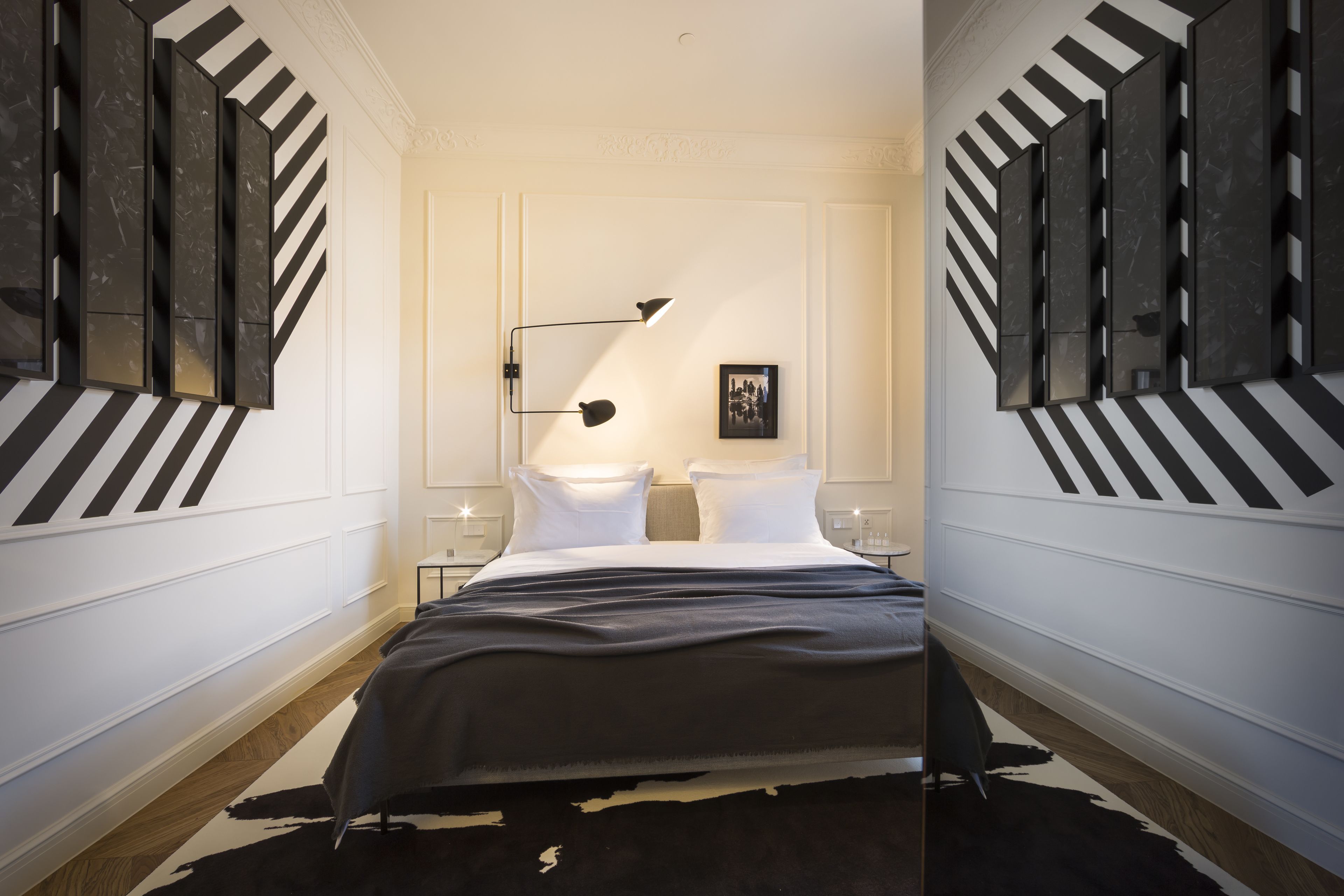 Una habitación de hotel moderna con una cama grande, dos mesitas de noche, un diseño de pared a rayas negras y blancas y un cuadro colgado.