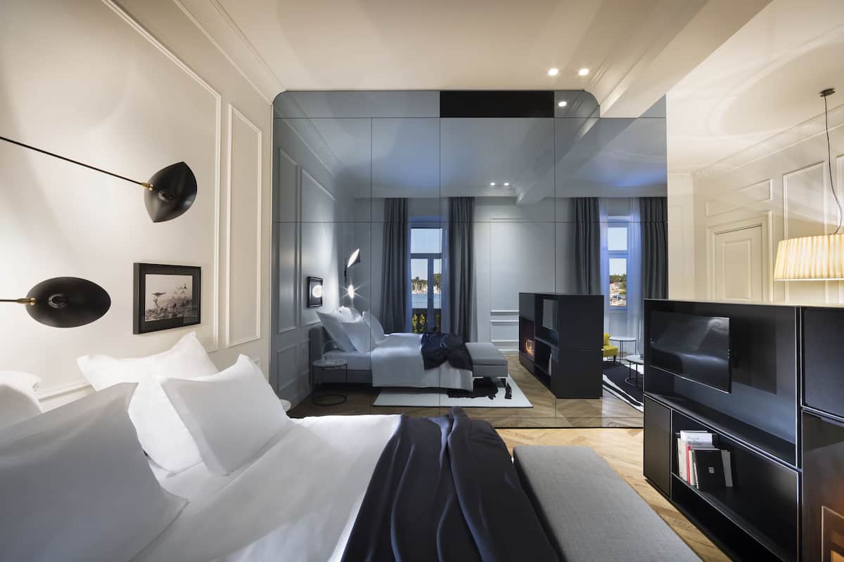 A modern hotel room with a bed, a sofa, a TV, and a fireplace.