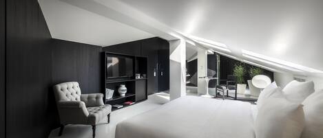 Un dormitorio moderno con una cama grande, una zona de estar con una silla y un televisor empotrado.