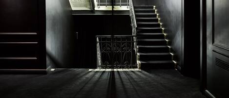 Un interior moderno con una escalera que sube a un nivel superior, con tragaluces y barandilla de metal.