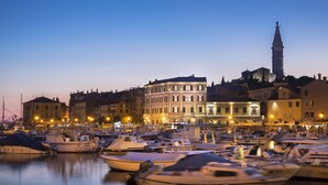 Un puerto deportivo con barcos amarrados, un edificio histórico con ventanas iluminadas y una torre al fondo.