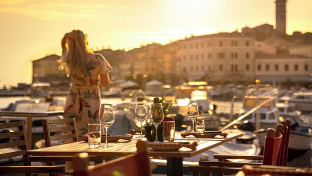 Una mesa de comedor con copas de vino y una botella, con vistas a un puerto deportivo con barcos y edificios al fondo.