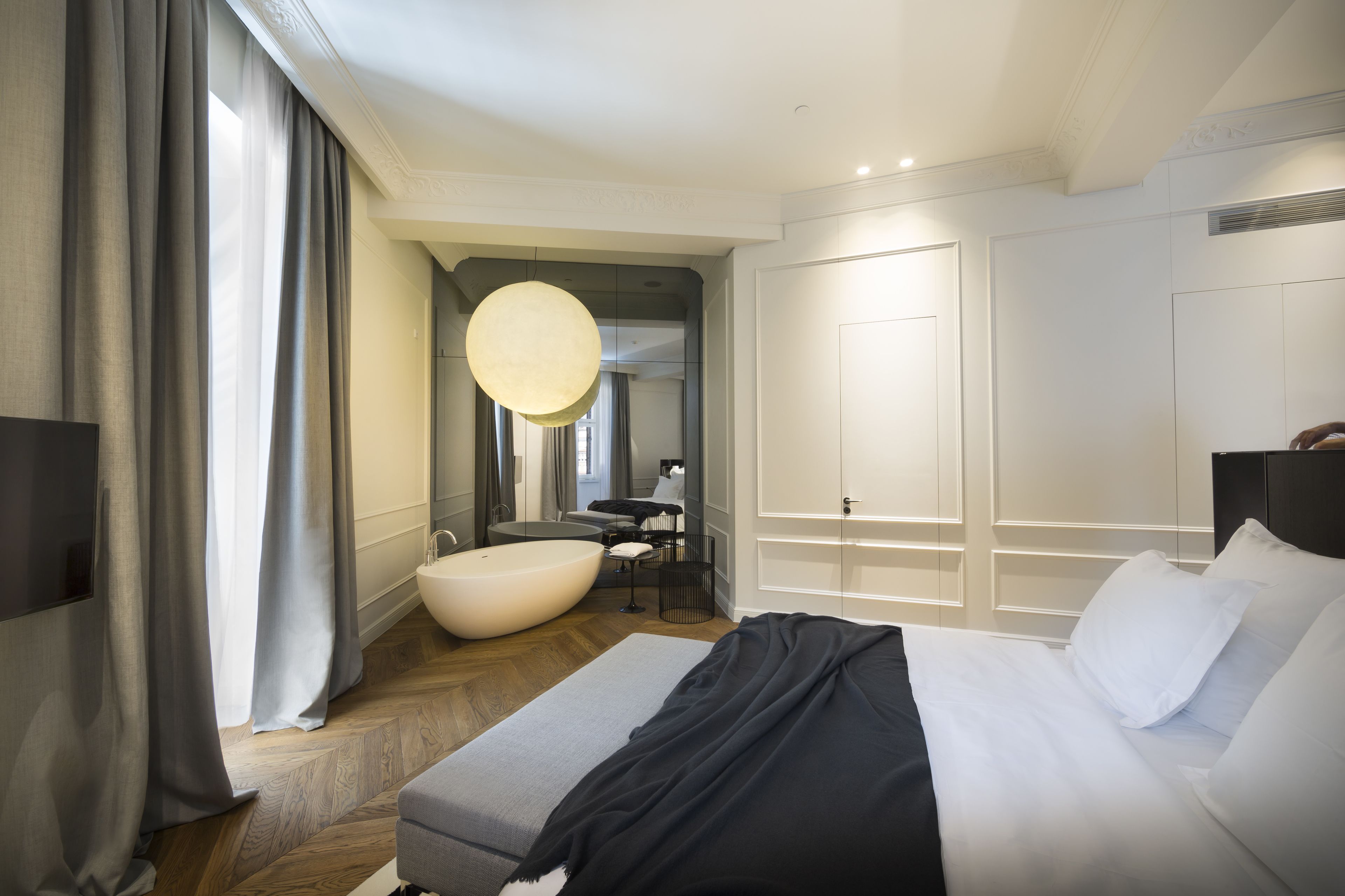 Una habitación de hotel moderna con una cama grande, un espejo redondo, una bañera y un escritorio con una silla.