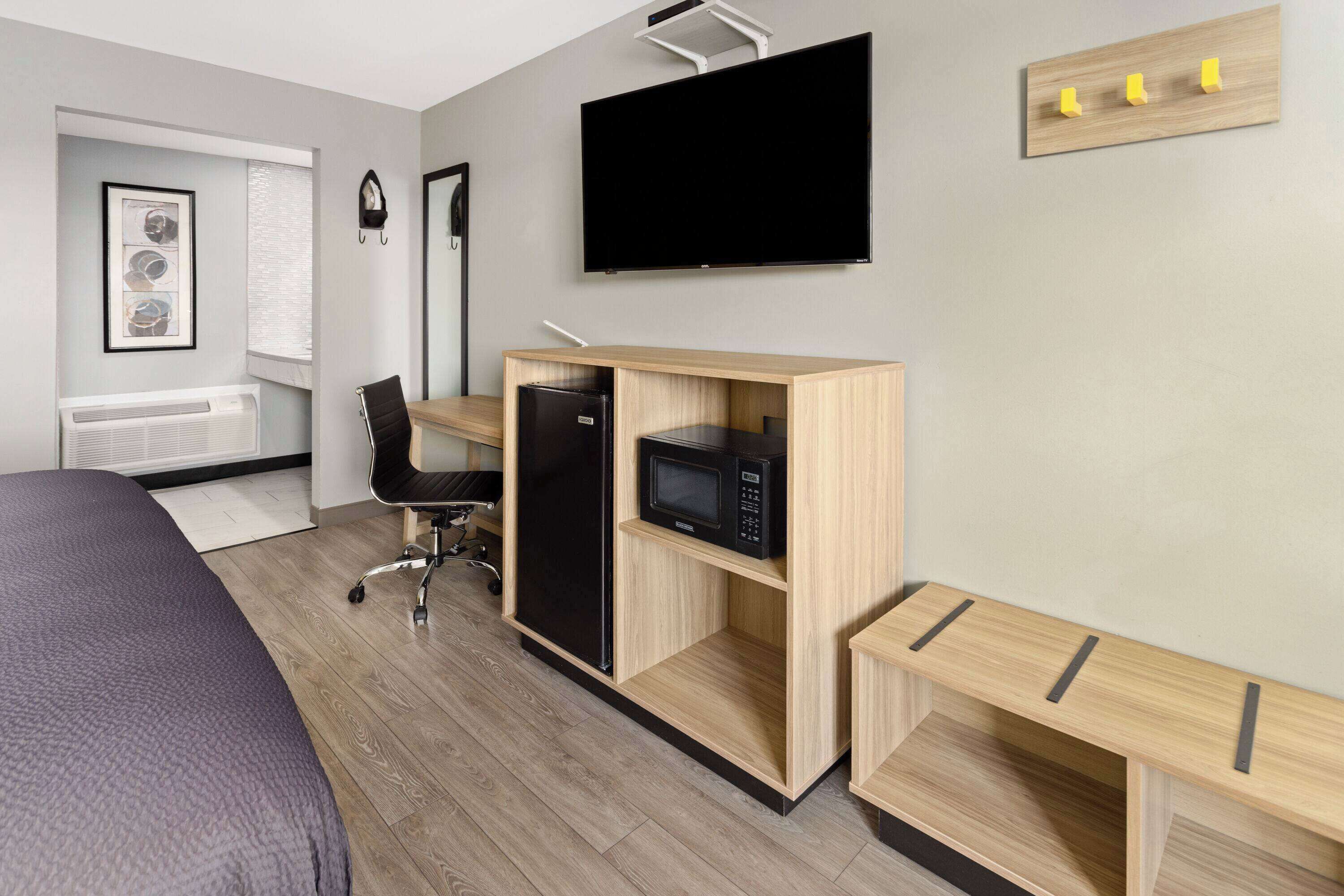Una habitación de hotel moderna con cama, escritorio, computadora, microondas, televisor y un pequeño espacio para sentarse.
