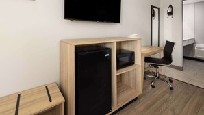 A modern hotel room with a wooden desk, a black refrigerator, a black office chair, a flat-screen TV mounted on the wall, and a large mirror. - Super 8 by Wyndham Hazleton (Hazleton)
