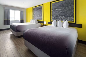 A hotel room with two beds, a large window with curtains, and two black-and-white landscape paintings on the wall.