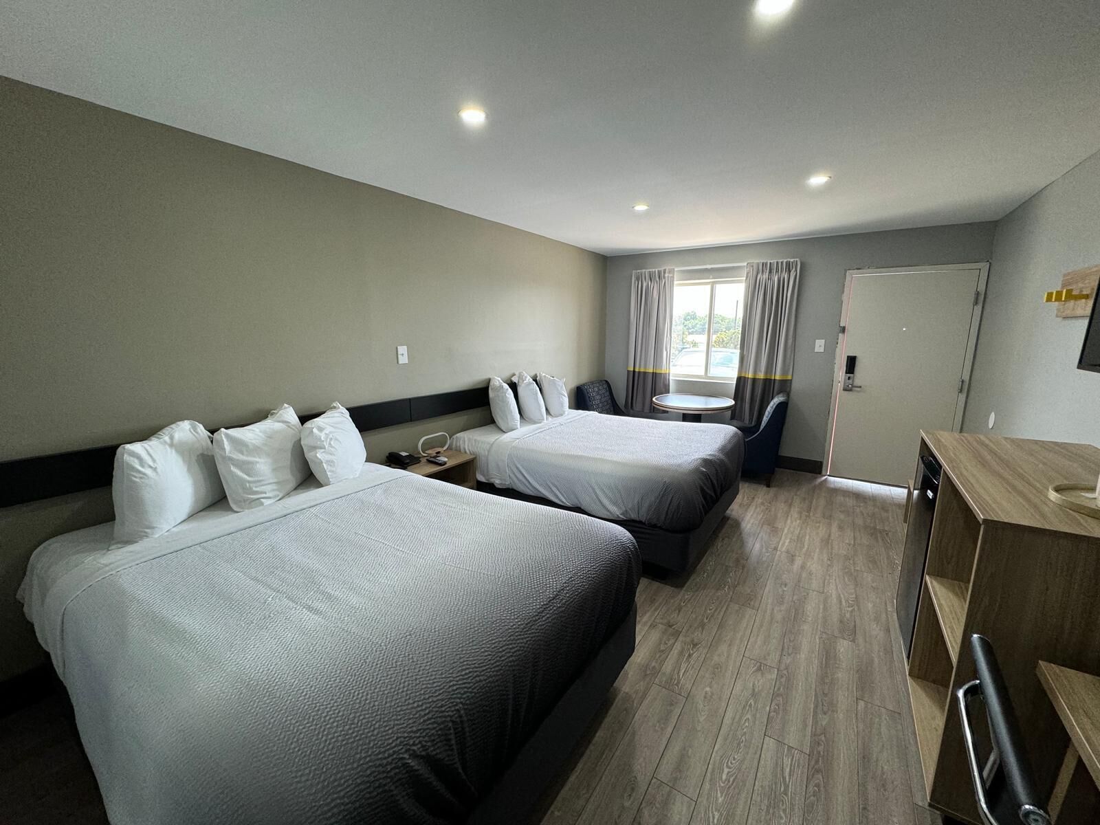 A hotel room with two beds, a desk, a chair, a small table, and a window with curtains.