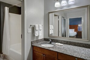 A bathroom with a granite countertop sink, a mirror, and a shower curtain.