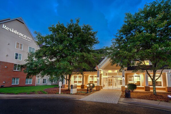 A hotel entrance with a brick facade, large windows, and a well-lit entrance area.