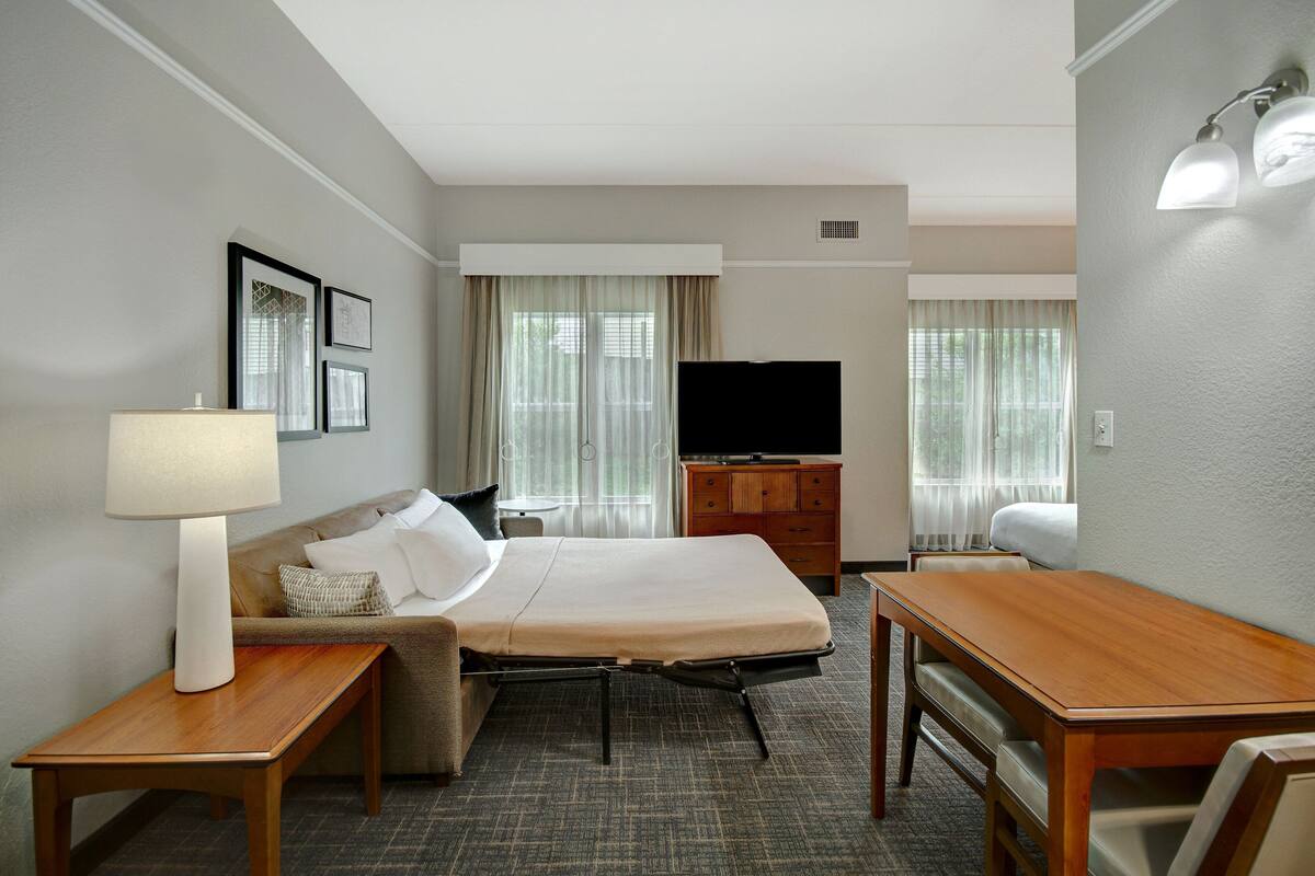 A hotel room with a bed, a desk, a chair, a television, and a lamp.