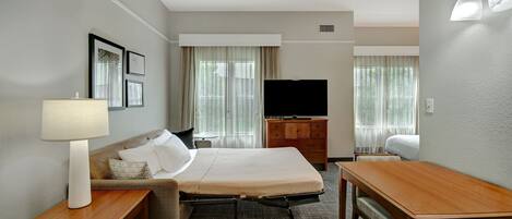 Habitación de hotel con cama, escritorio, silla, televisor y lámpara.
