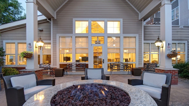 An outdoor patio area with a circular stone fire pit, wicker furniture, and hanging planters. - Residence Inn by Marriott Morgantown Medical Center Area (Morgantown)