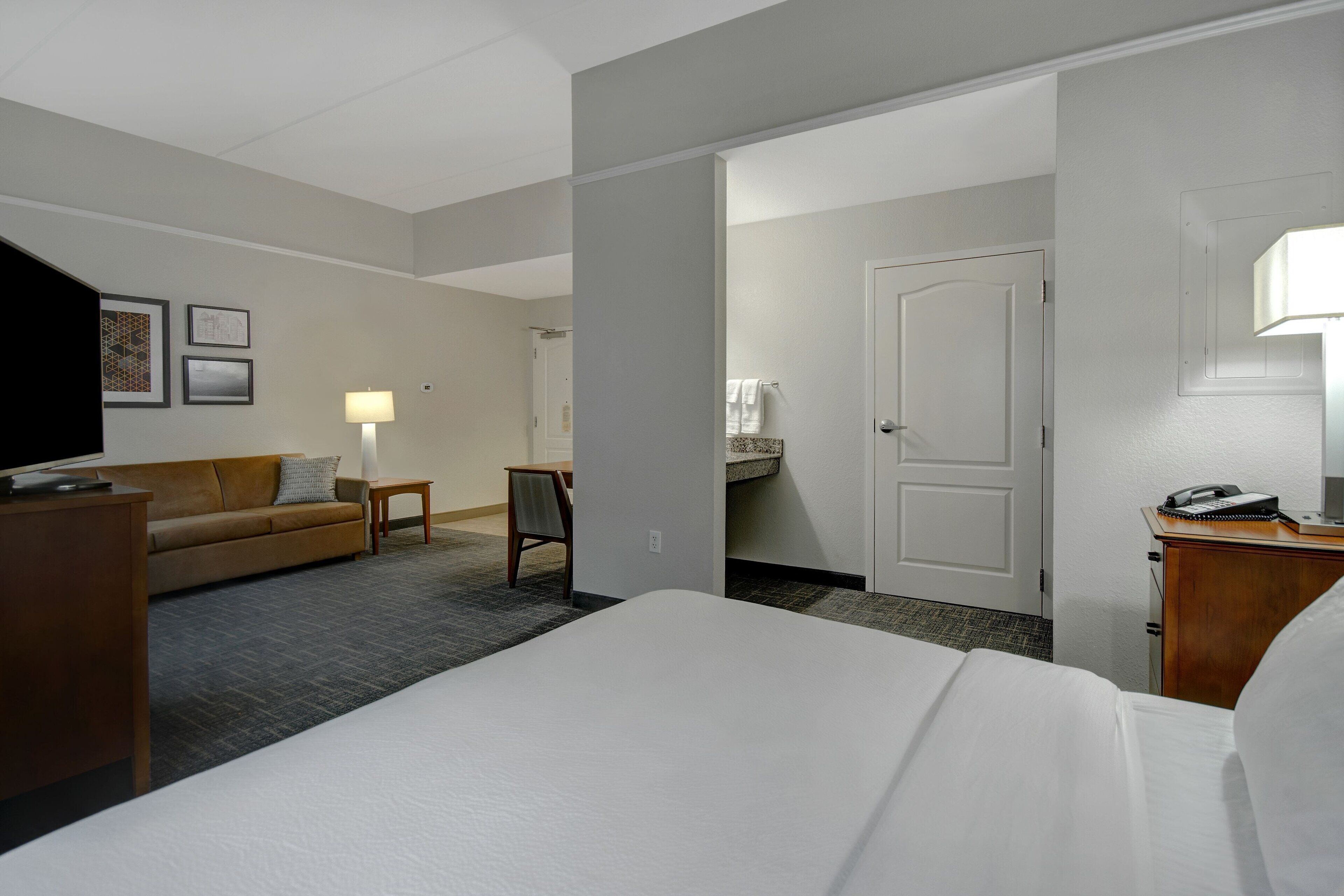 A hotel room with a bed, a sofa, a desk, a lamp, and a television.