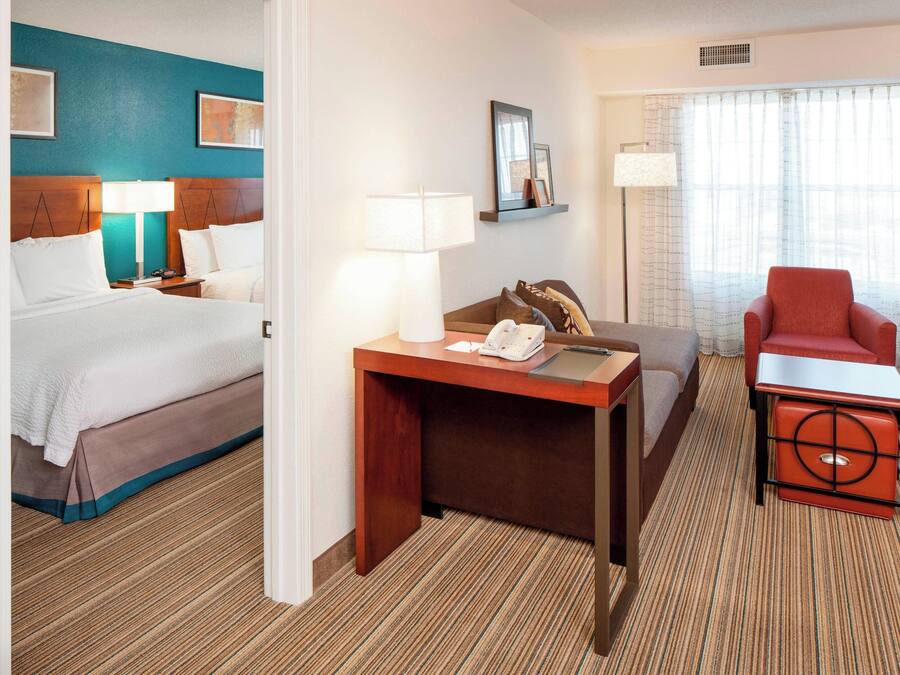 Una habitación de hotel con cama, escritorio, teléfono, silla y lámpara.