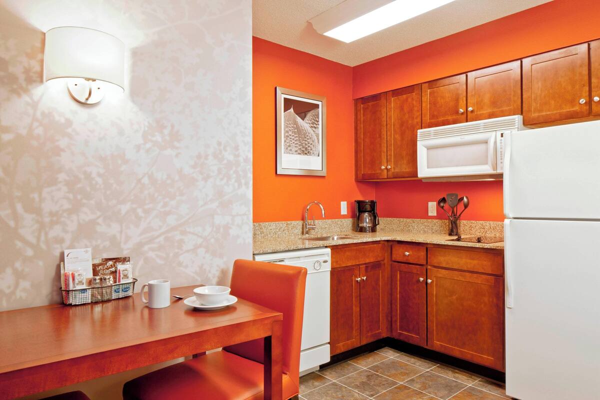 A compact kitchen with wooden cabinets, a white refrigerator, a microwave, and a coffee maker.