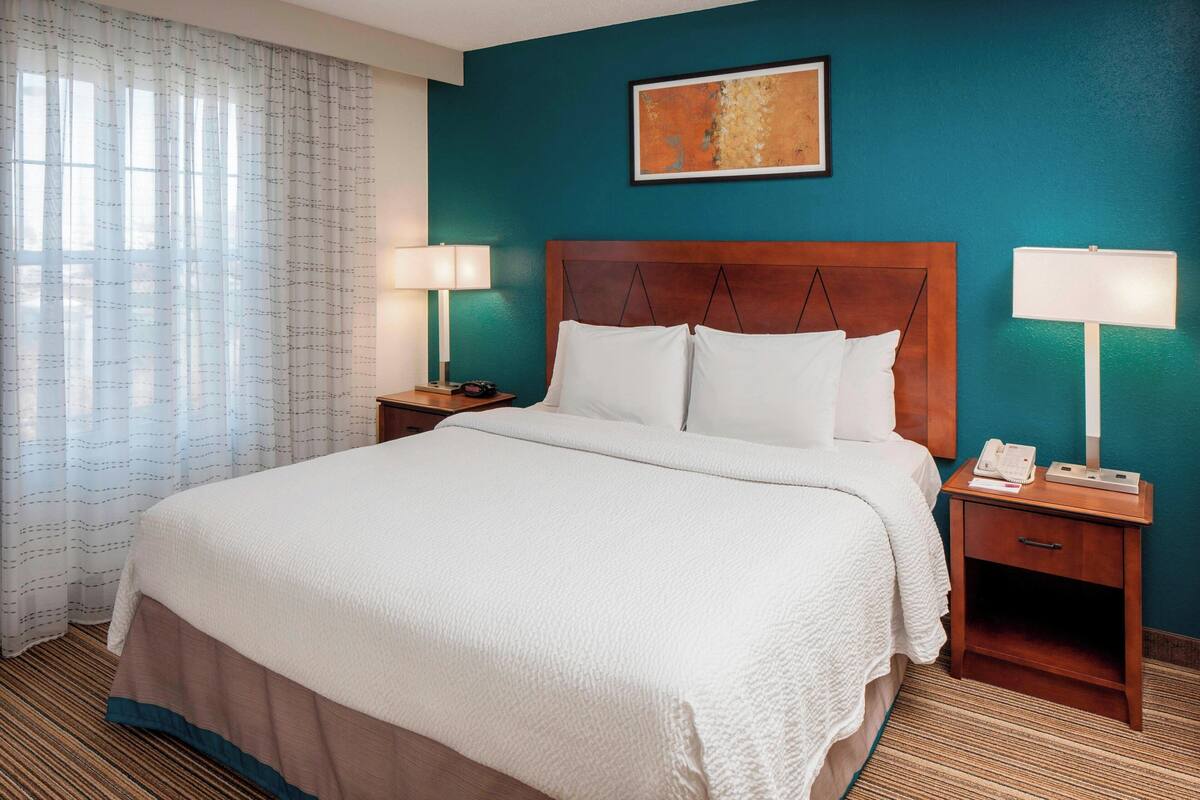 A hotel room with a large bed, two bedside tables, a nightstand, a telephone, and a painting on the wall.