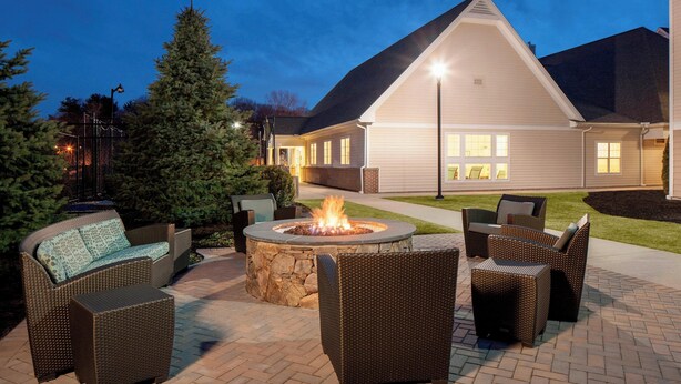 Une terrasse extérieure avec des meubles en osier, un foyer en pierre et une maison en arrière-plan.