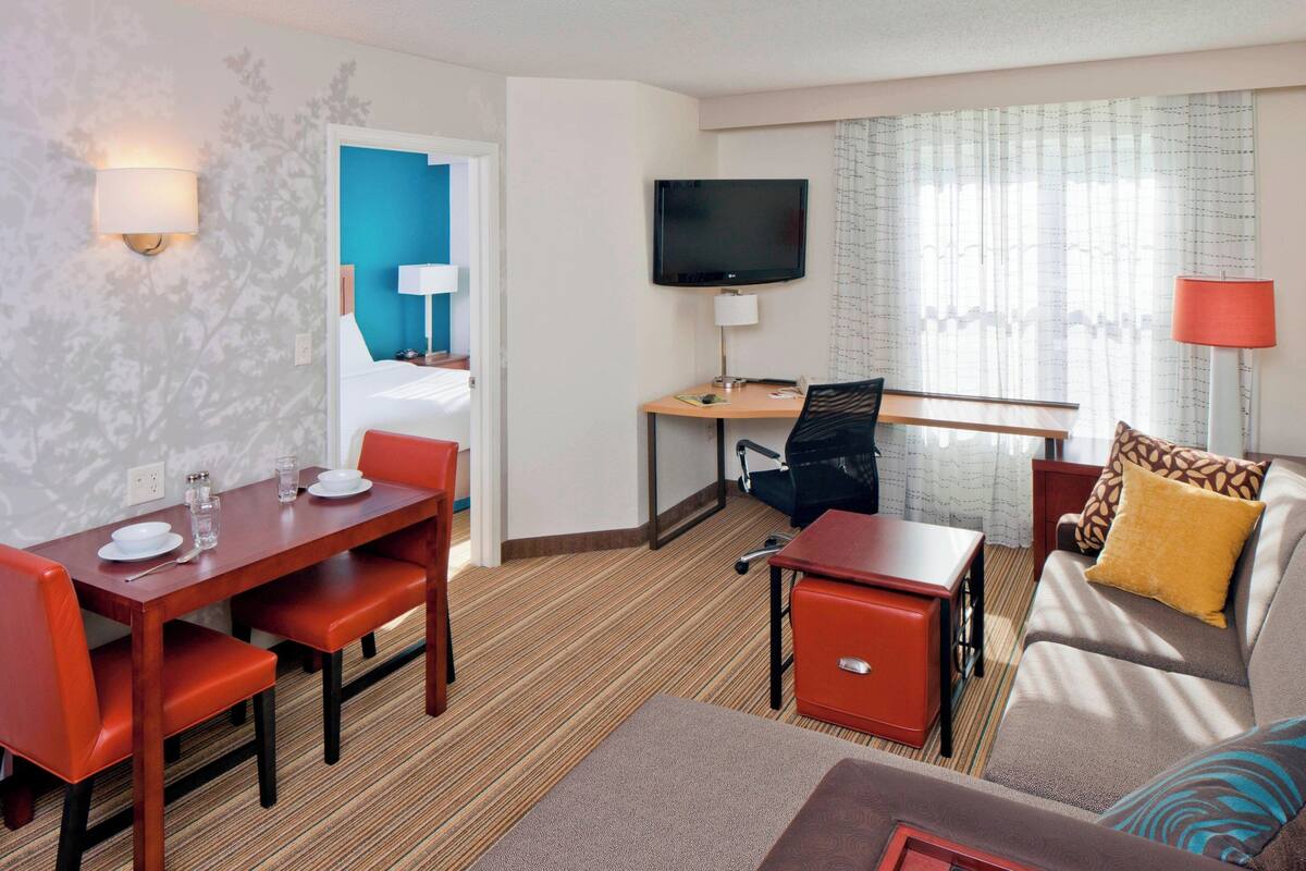 A hotel room with a dining table, chairs, a sofa, a TV, and a desk.