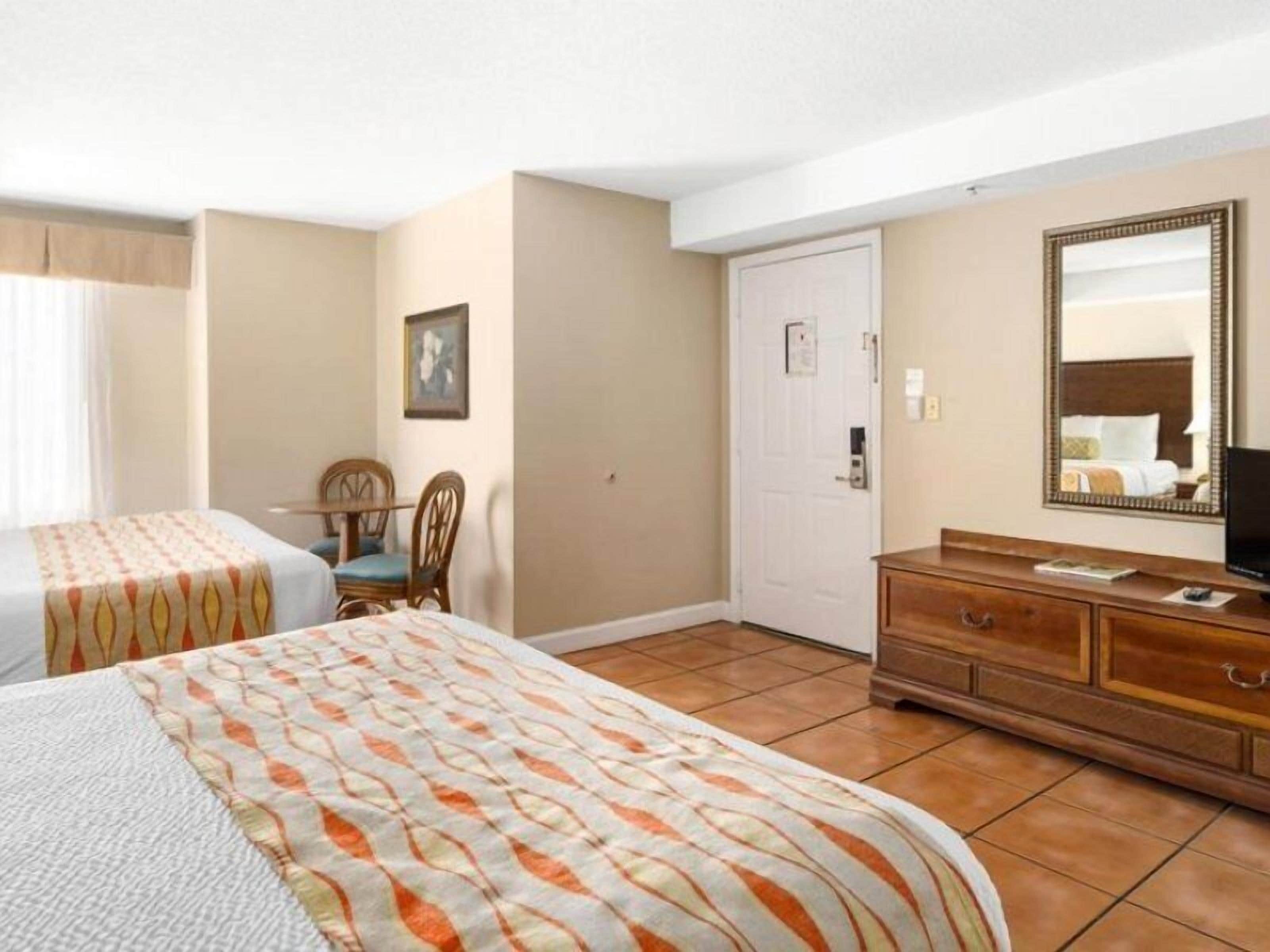 Une chambre d’hôtel avec deux lits, une commode en bois, un téléviseur et une porte.