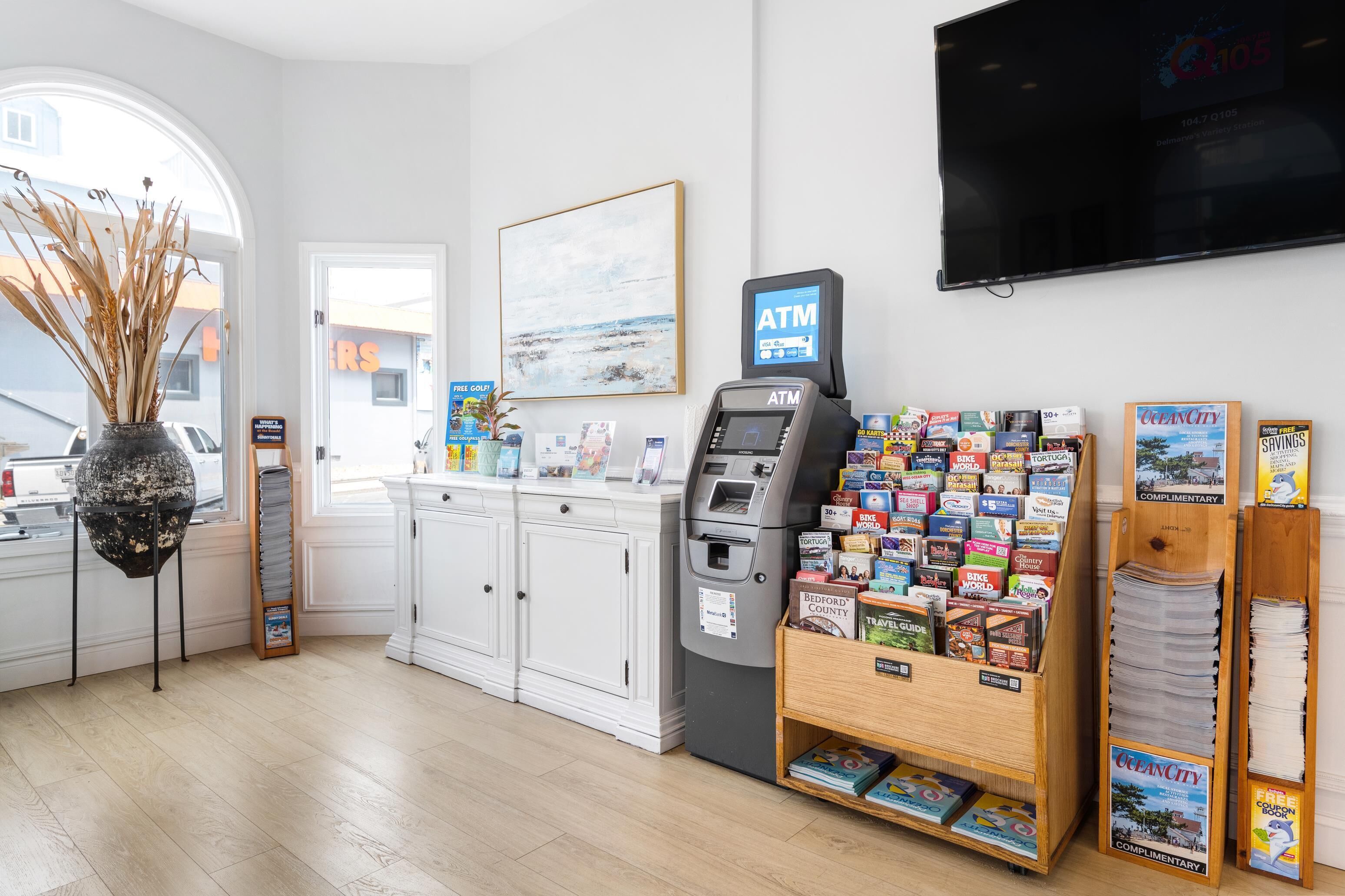 A reception area with a white counter, an ATM, a magazine rack, and a TV on the wall.