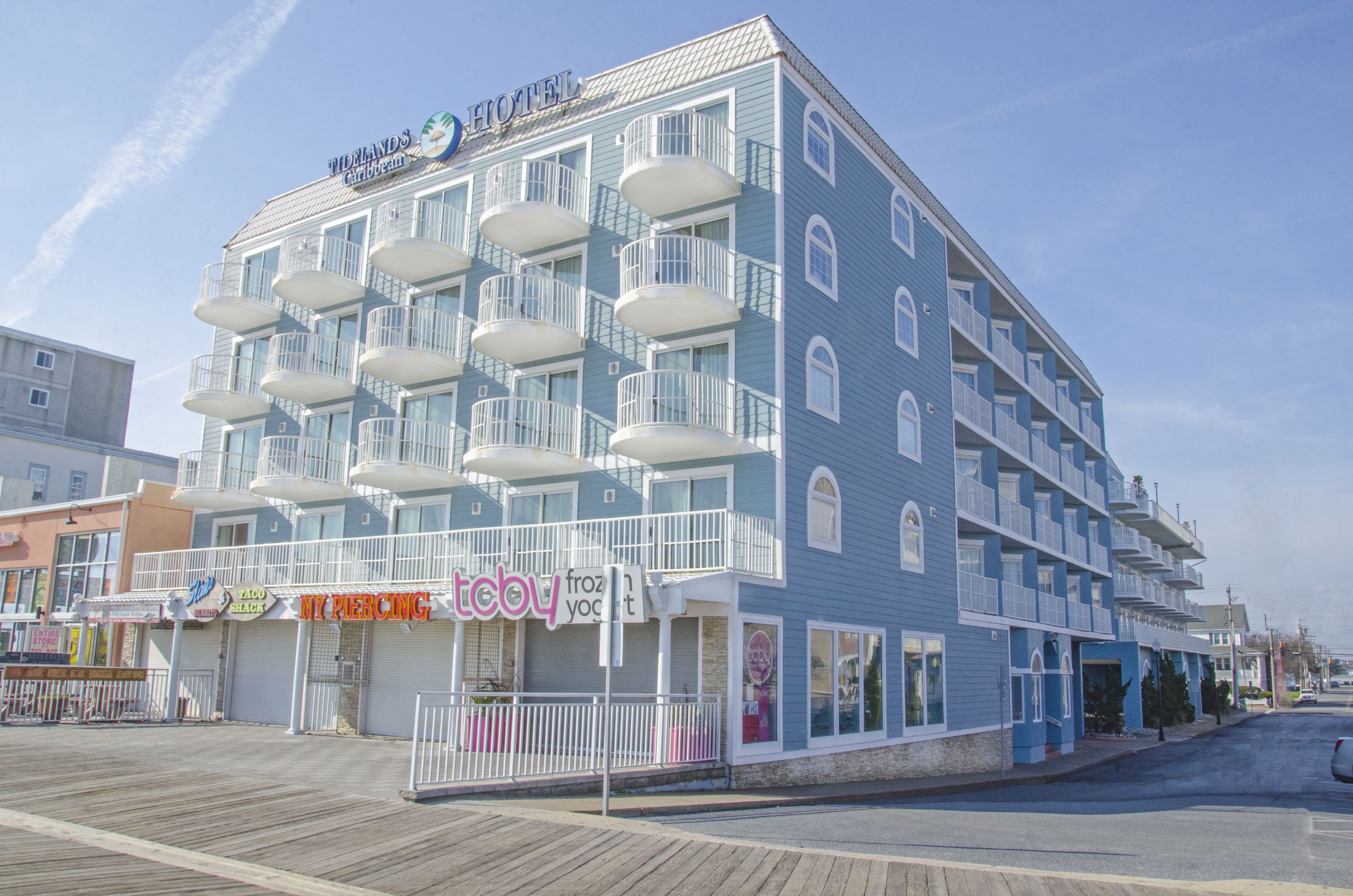 Un hôtel doté de nombreux balcons, une promenade en bord de mer devant, et diverses boutiques, dont un salon de piercing et un magasin de yaourts glacés.