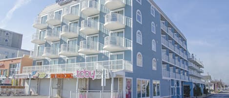 Um hotel com várias varandas, uma passarela em frente e diversas lojas, incluindo uma loja de piercings e uma sorveteria de iogurte.