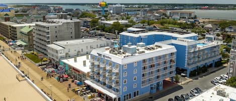 A coastal cityscape with a prominent blue hotel featuring balconies and a rooftop pool.