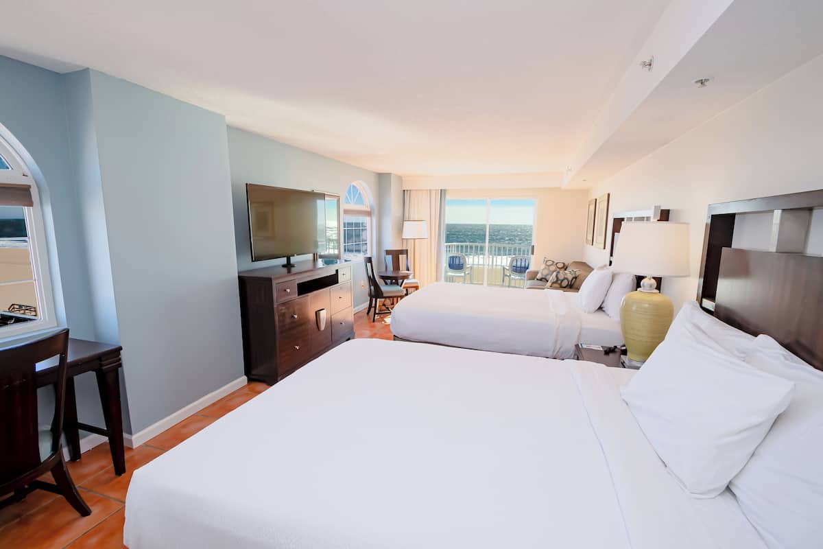 Ein Hotelzimmer mit einem großen Bett, einem Schreibtisch, einem Fernseher und einem Balkon mit Aussicht.