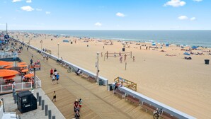 Une plage avec une promenade en bord de mer, des parasols et des personnes qui se prélassent au soleil.