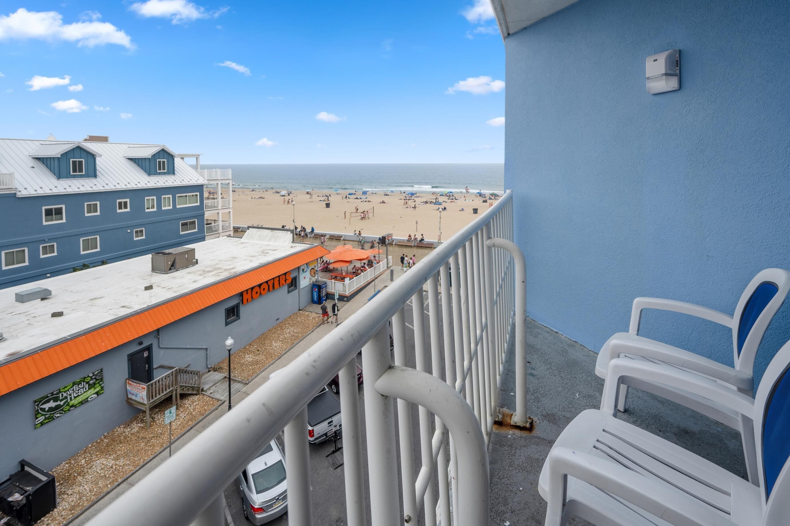 Ein Balkon mit Blick auf einen Strand, ein Gebäude mit der Aufschrift 'HOSTERS' und ein geparktes Auto.