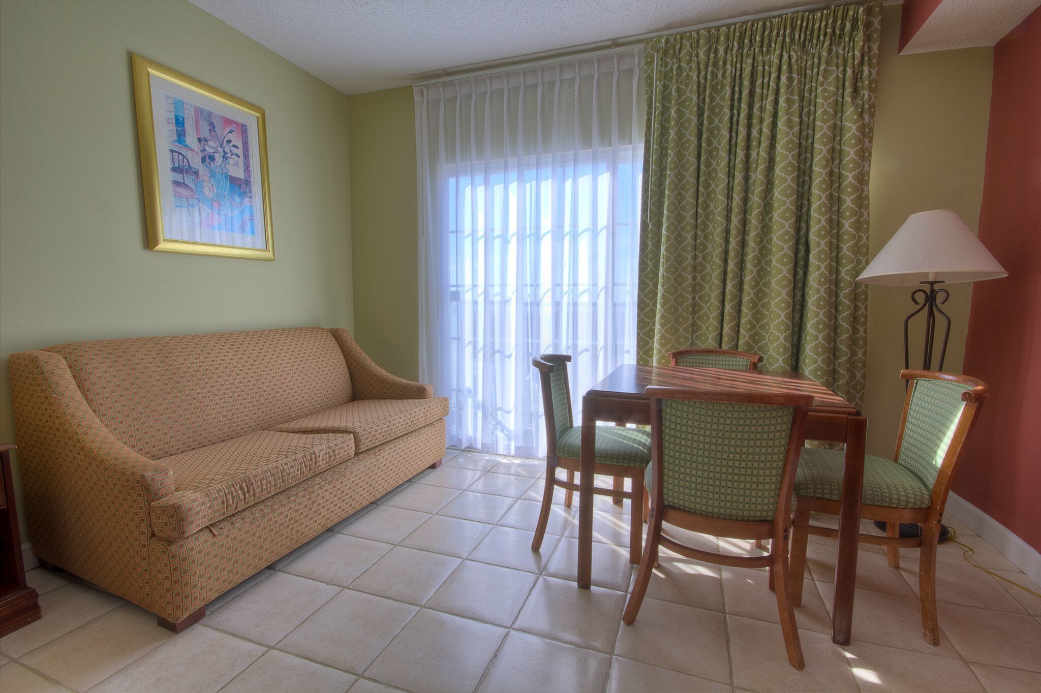 A living room with a sofa, dining table, chairs, a lamp, and a window with curtains.