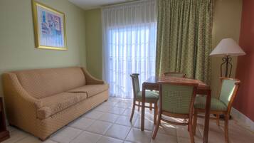 A living room with a sofa, dining table, chairs, a lamp, and a window with curtains.