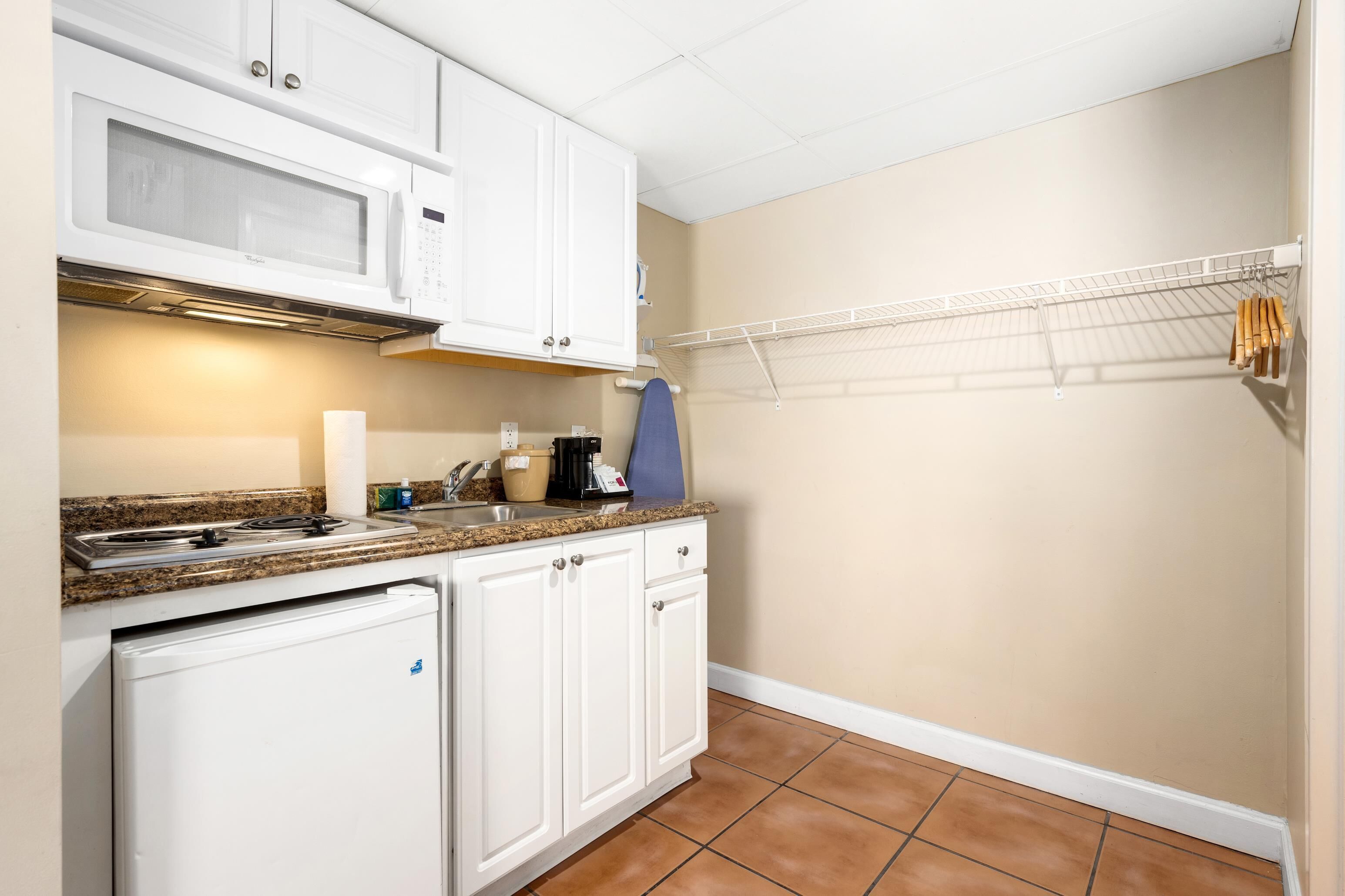 A compact kitchen with white cabinets, a microwave, a stove, and a drying rack.