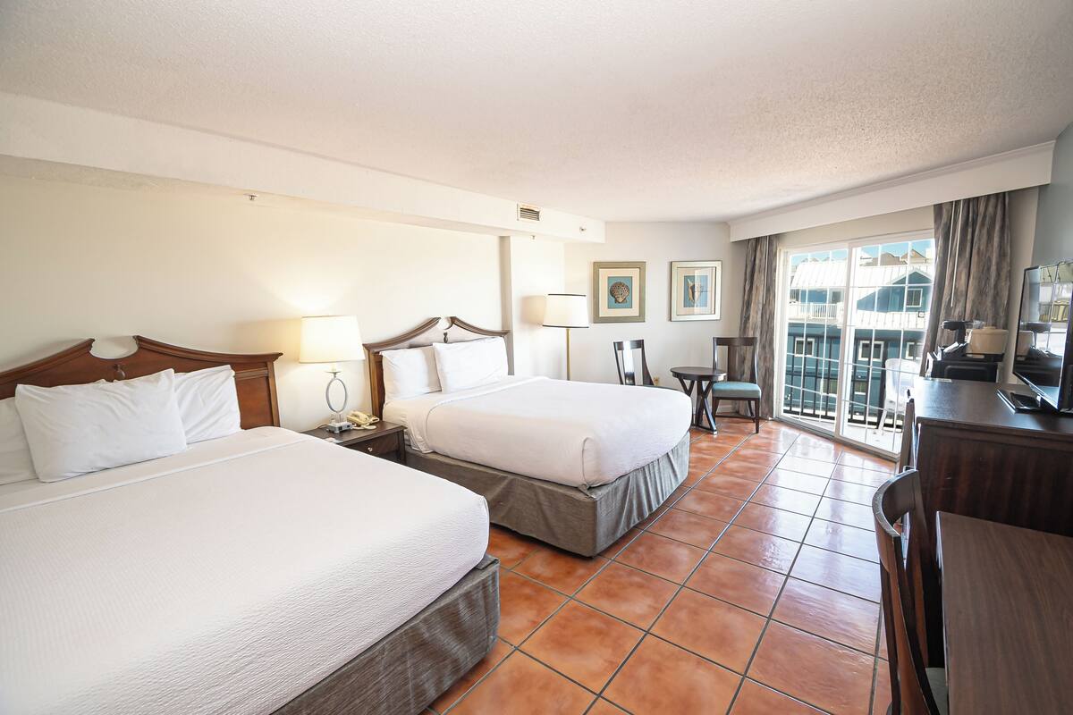 Ein Hotelzimmer mit zwei Betten, einem Schreibtisch, einem Stuhl und einem Balkon mit Blick.