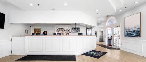 A spacious reception area with a large white reception desk, a flat-screen TV, and a refrigerator.
