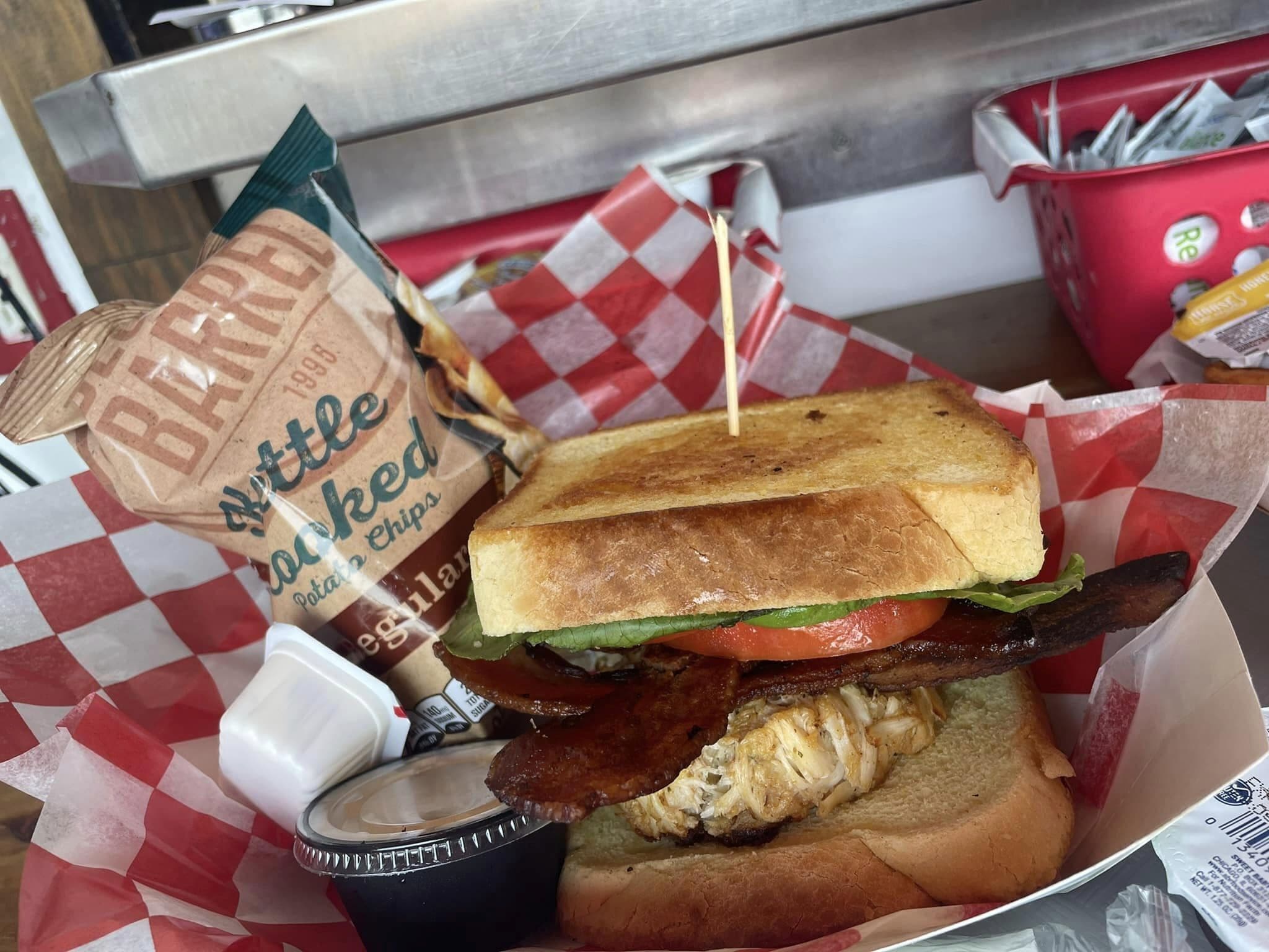 A sandwich with a toasted bun, lettuce, tomato, bacon, and a side of potato chips.