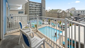Un balcon avec des chaises blanches, un espace piscine où une personne nage, et une vue sur les bâtiments environnants.