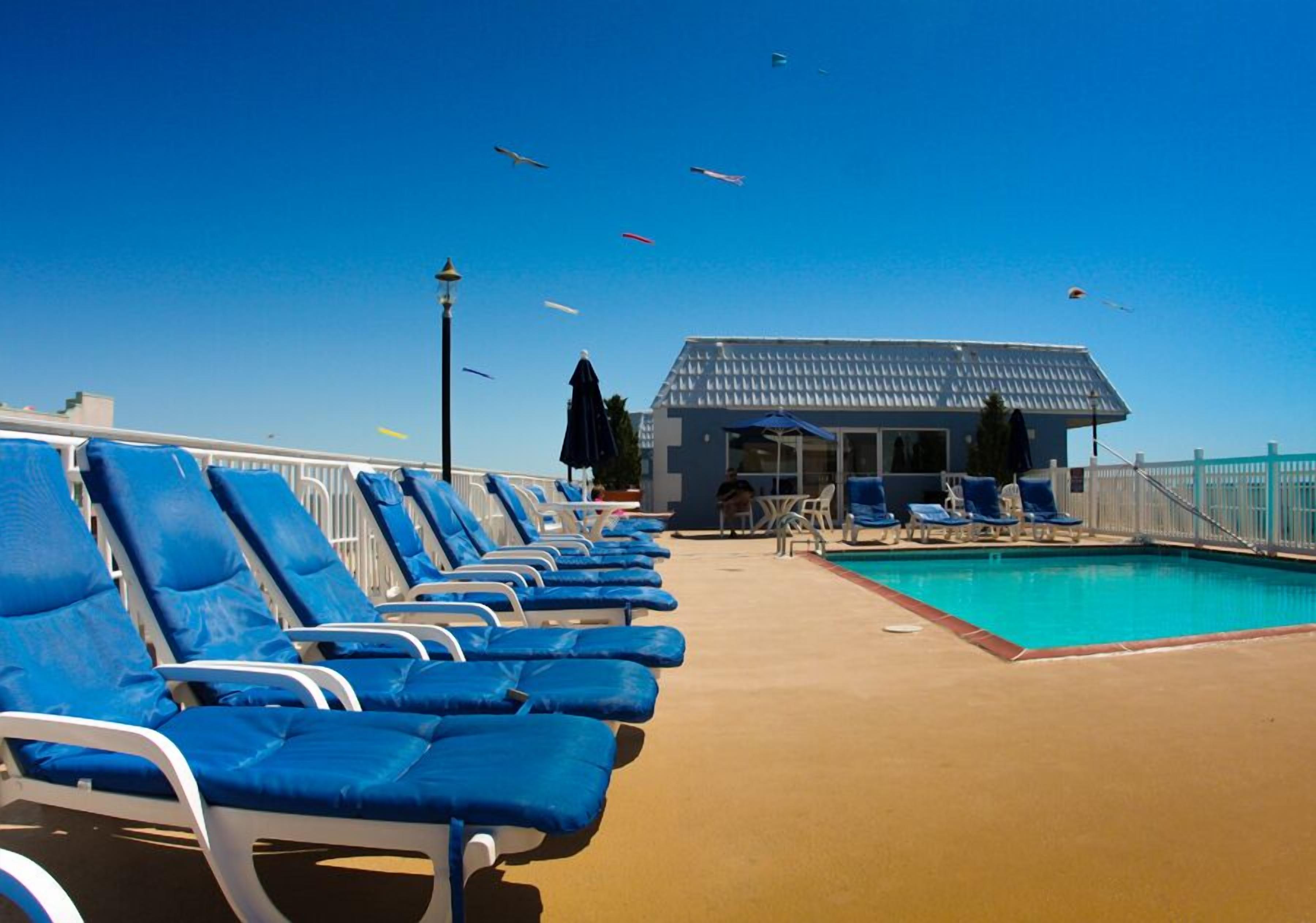 A poolside area with blue lounge chairs, a pool, and a building with a blue roof.