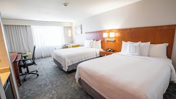 Een hotelkamer met twee bedden, een bureau, een stoel en een raam met gordijnen.