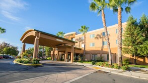 A hotel with a covered entrance, palm trees, and a parking lot. - Courtyard by Marriott Merced (Merced)