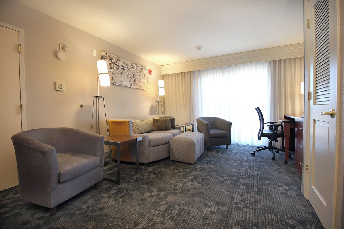 Une chambre d’hôtel équipée d’un canapé, d’un fauteuil, d’un pouf, d’un bureau et d’une chaise.
