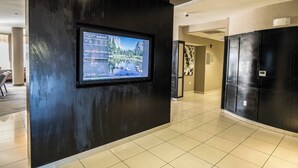 A modern hotel lobby with a digital display on the wall, tiled flooring, and a reception area. - Courtyard by Marriott Merced (Merced)