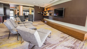 A modern lounge area with a flat-screen TV mounted on the wall, a sofa, and a coffee table. - Courtyard by Marriott Merced (Merced)