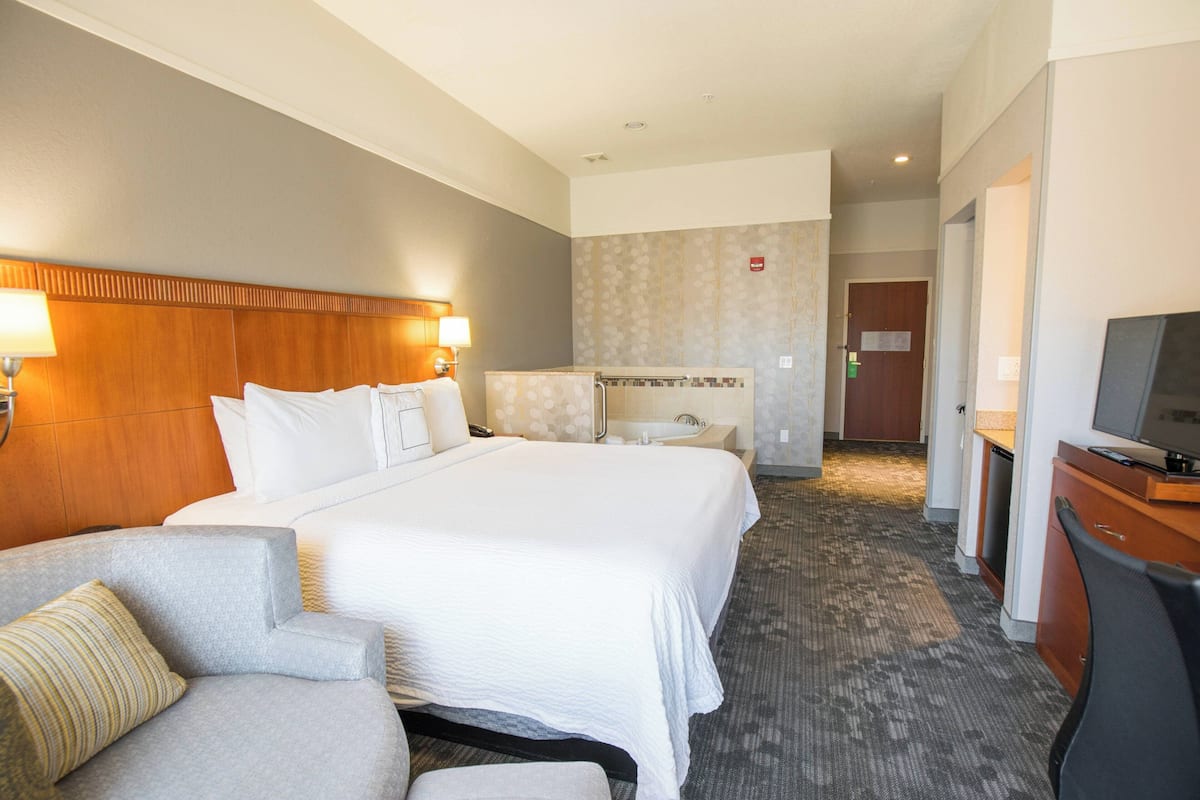 Une chambre d’hôtel avec un grand lit, un bureau avec une télévision, une chaise et une salle de bain équipée d’une baignoire et d’une douche.