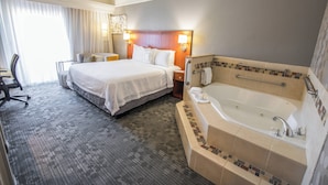 A hotel room with a large bed, a sitting area with a chair, a desk, and a bathroom with a bathtub and a shower. - Courtyard by Marriott Merced (Merced)