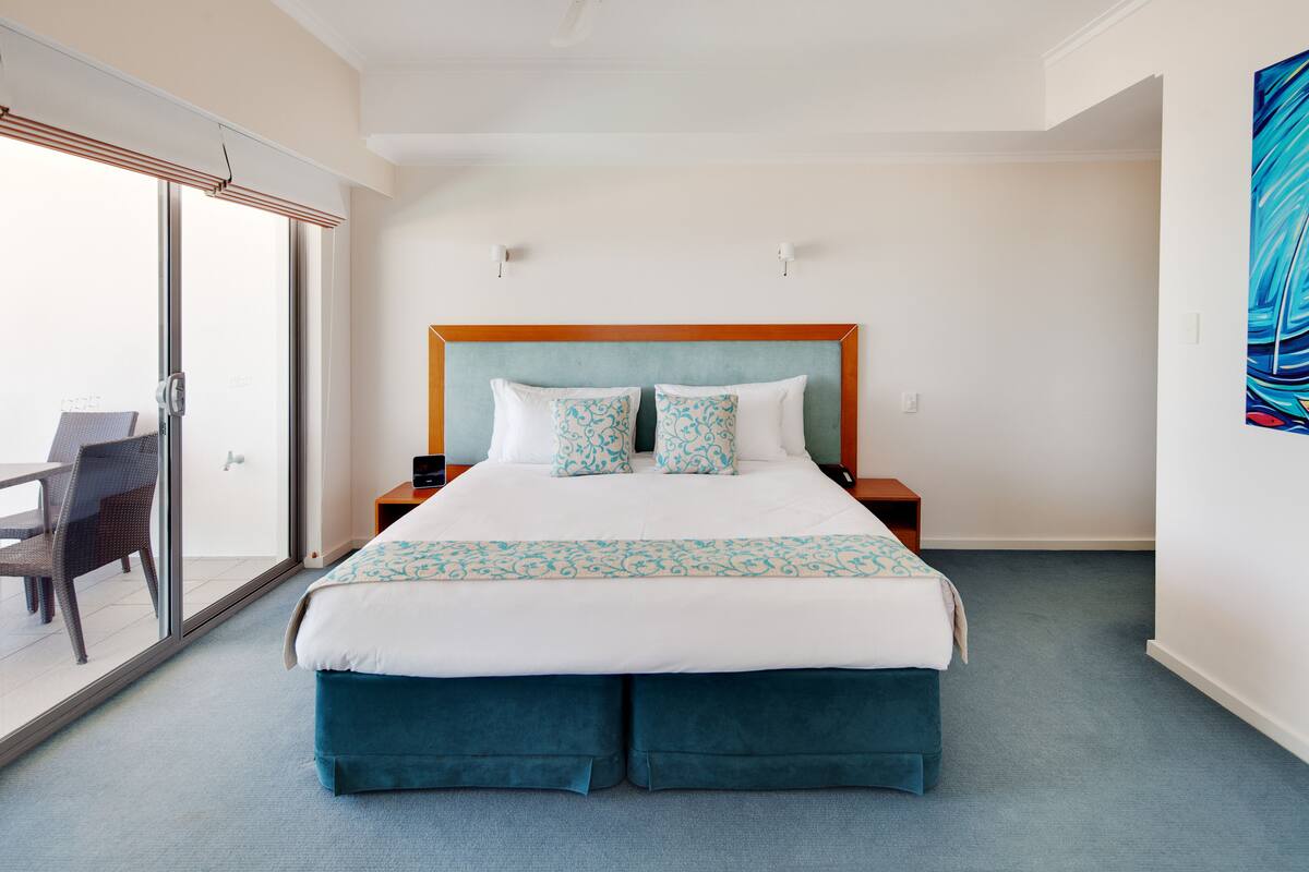 A hotel room with a large bed, a balcony with wicker furniture, and a painting on the wall.