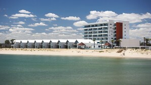 Un hotel frente a la playa con varios niveles, piscina y vistas a la playa.